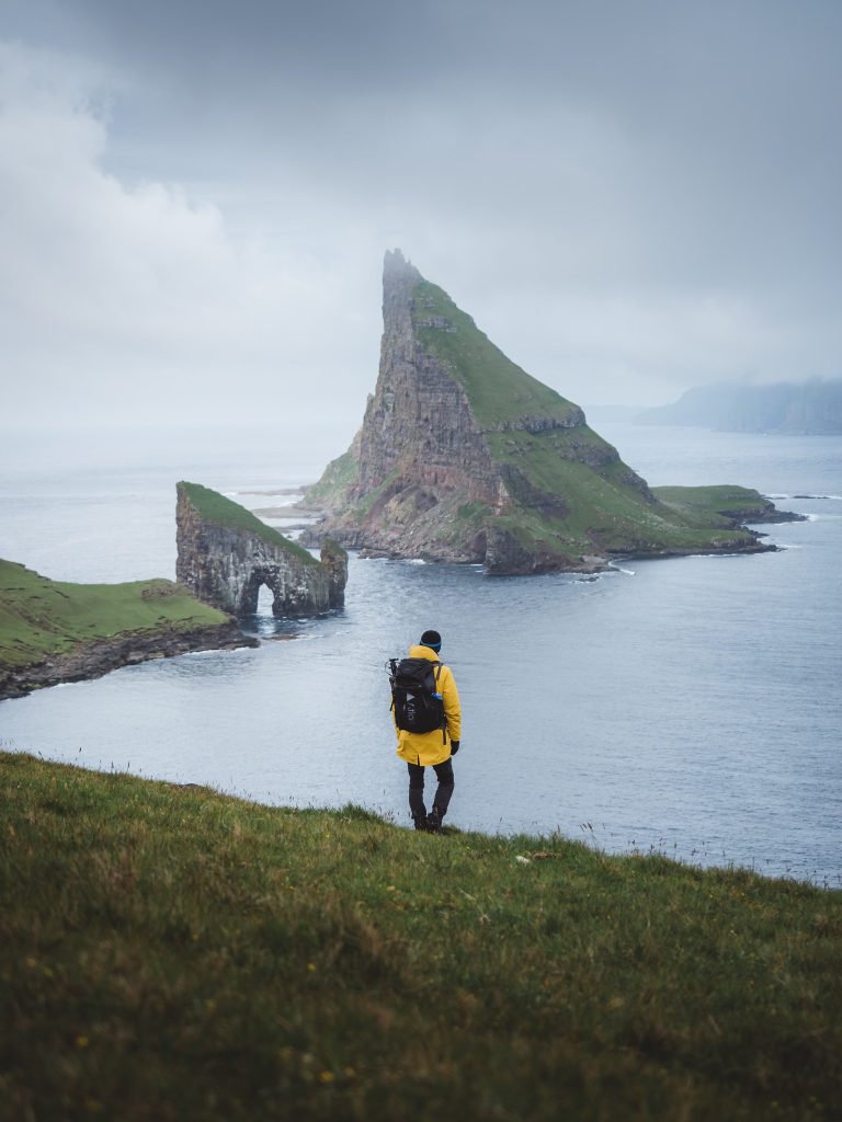 Mand i gul jakke står på bakke med udsigt over havet og klipper.
