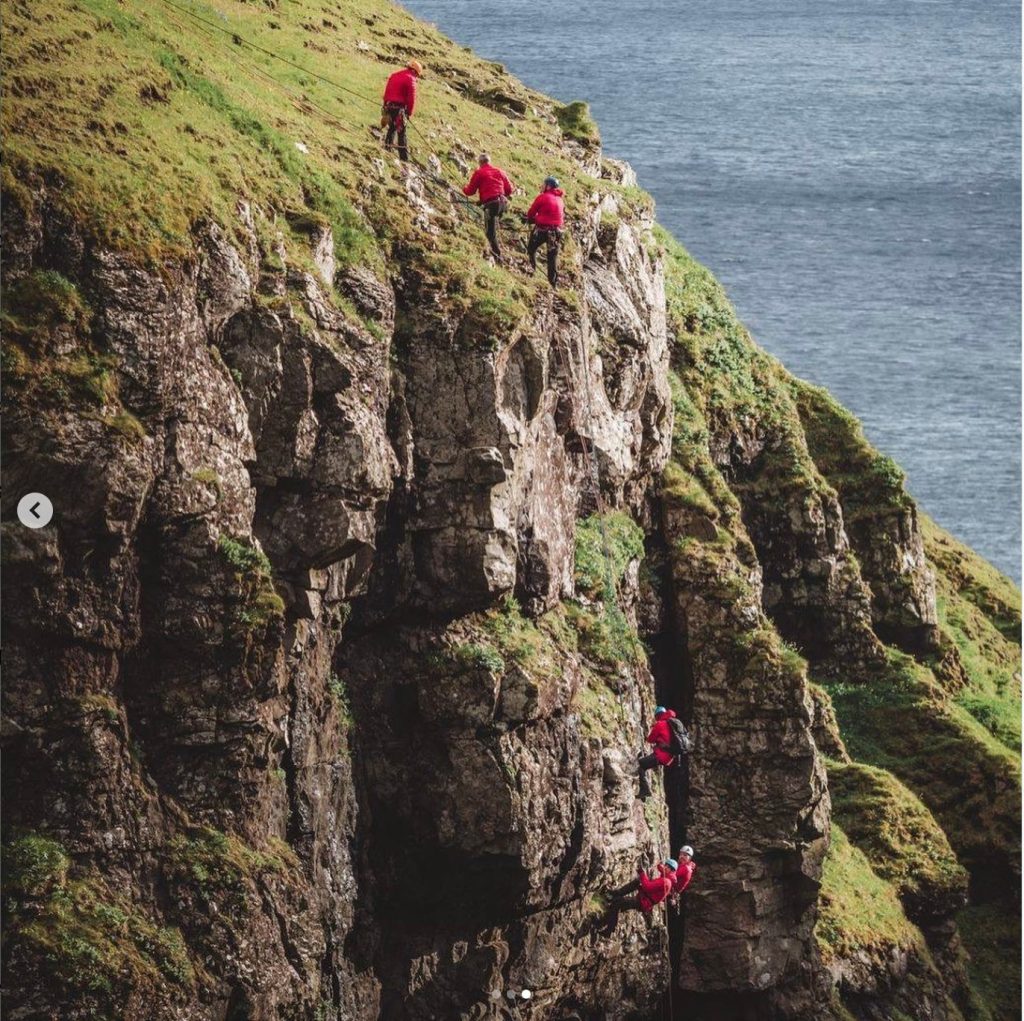 Personer, der klatrer op ad en klippe nær havet.